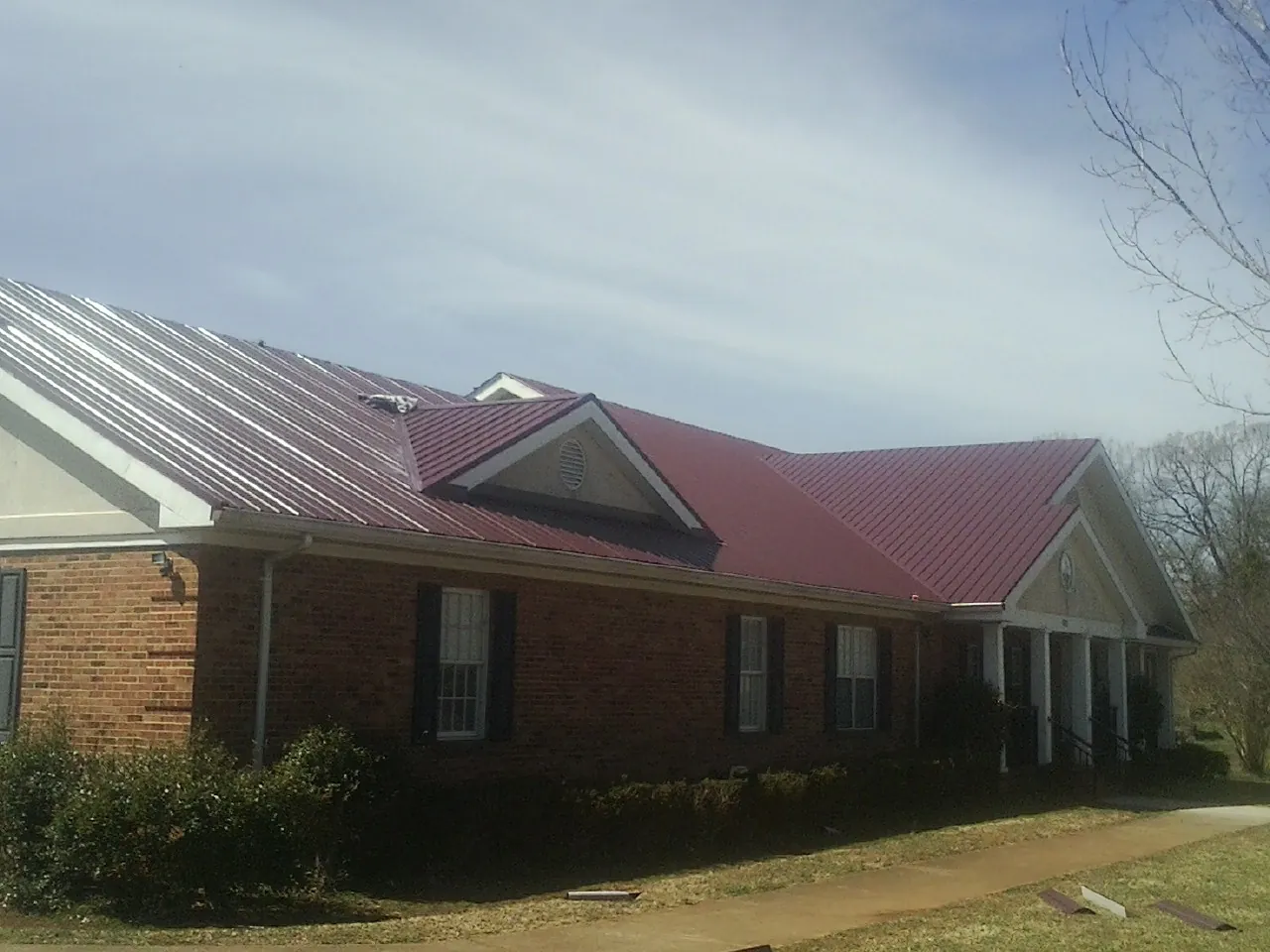 Red metal roof with gabled entries on a long brick building, from a Hail Damage Roof Repair job in Burlington
